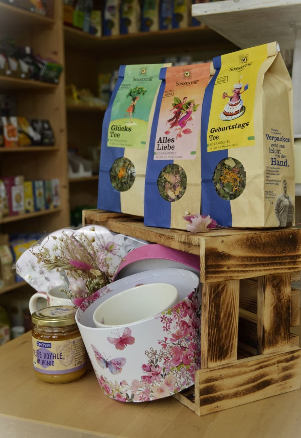 Drei Beutel Tee stehen auf einem Holzregal neben einem Glas Honig.