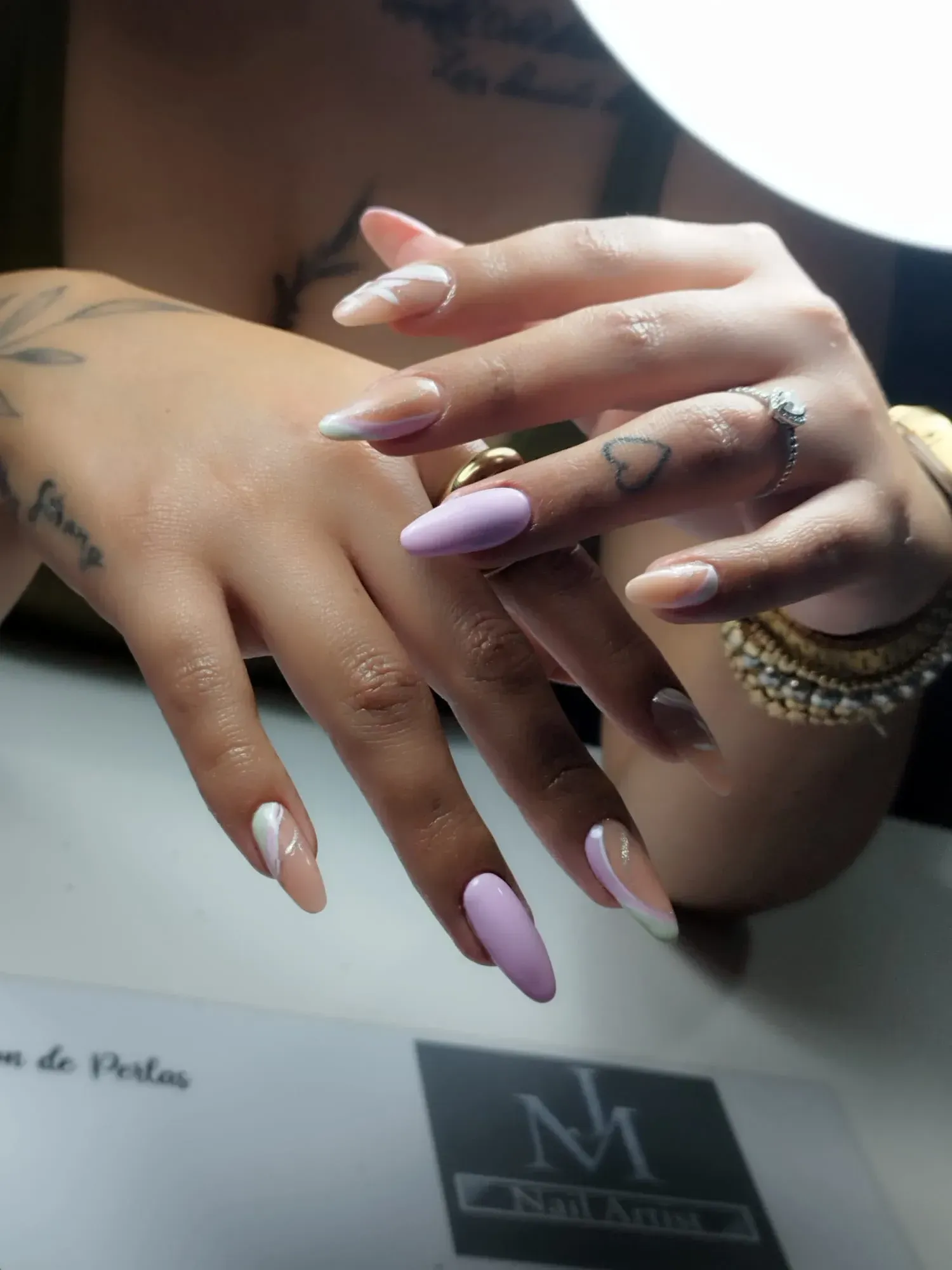 Manos con uñas en forma de almendra en tonos lavanda y nude con diseños de acentos blancos