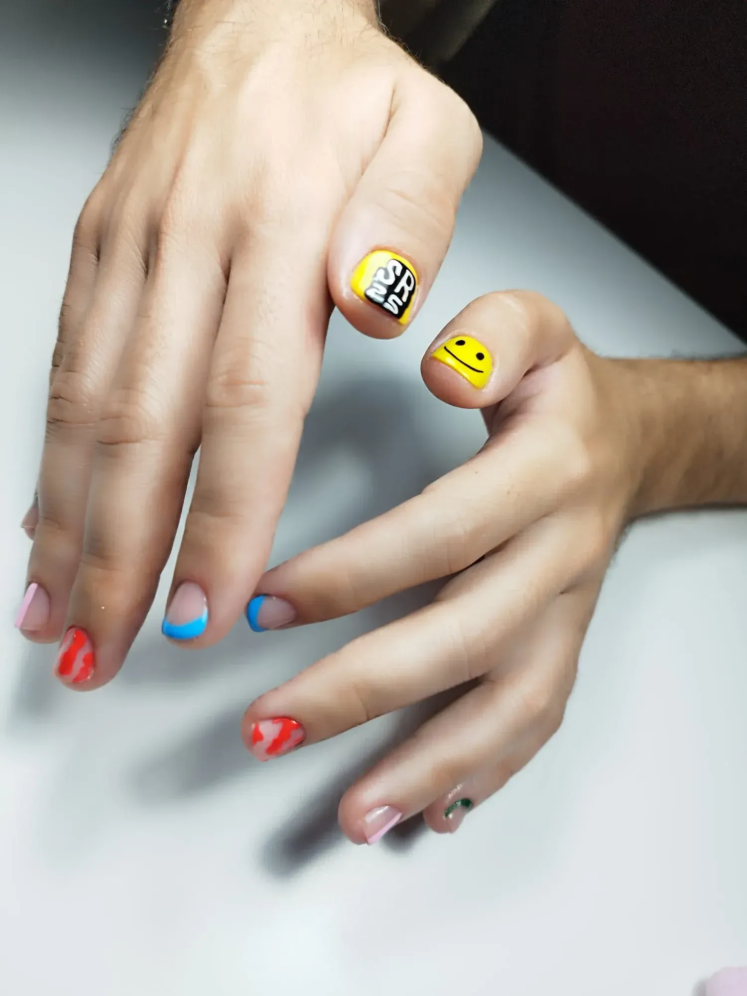 Manos con uñas decoradas de colores; rojo, azul, amarillo y caras sonrientes.