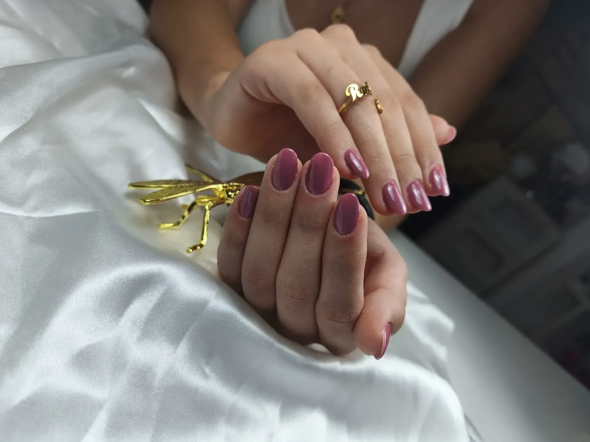 Manos con uñas cuidadas de color malva; un anillo de oro; descansando sobre tela de satén blanco.