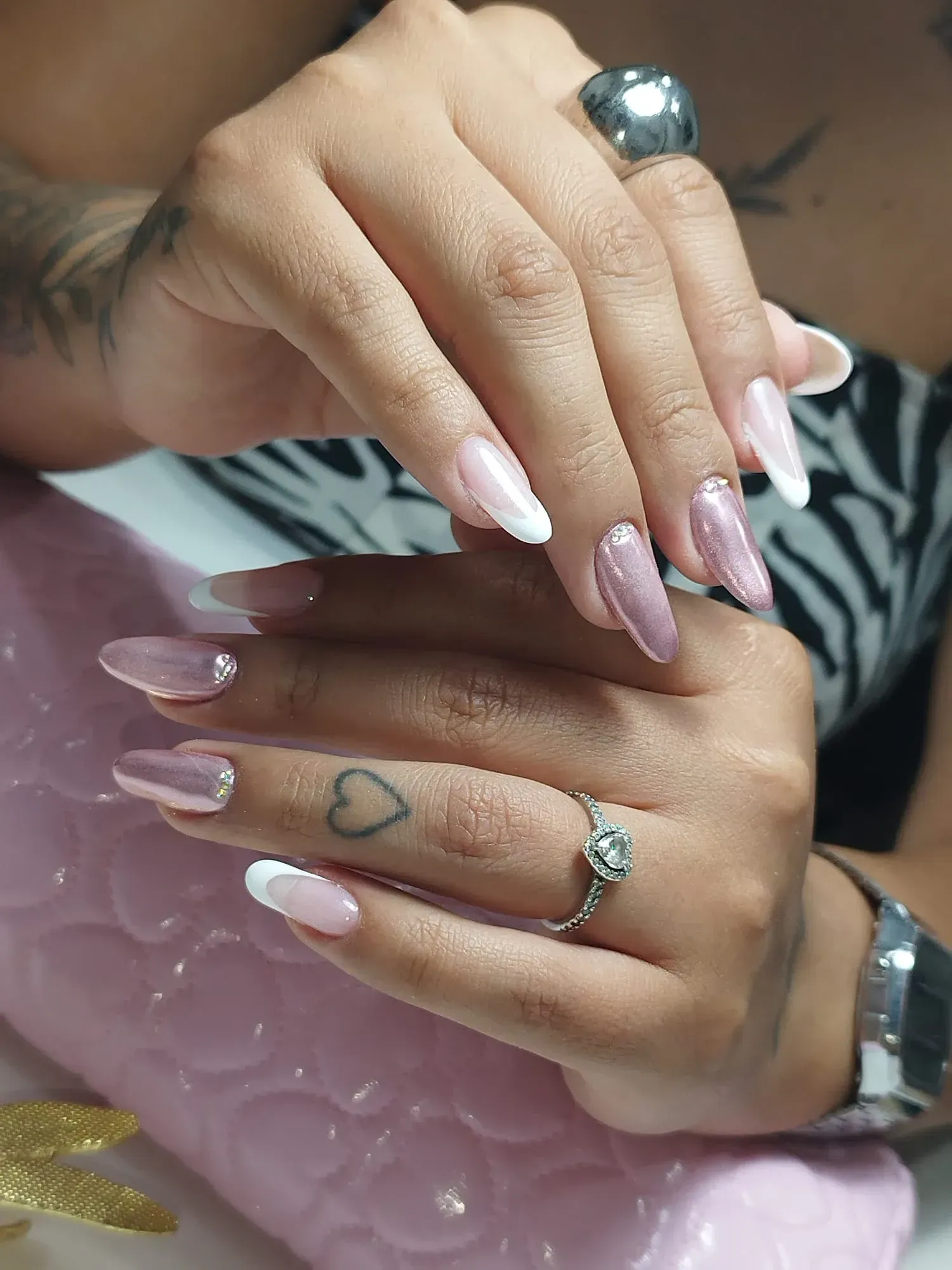 Manos con uñas largas pintadas en varios tonos rosas y puntas francesas, adornadas con anillos y un reloj de pulsera.