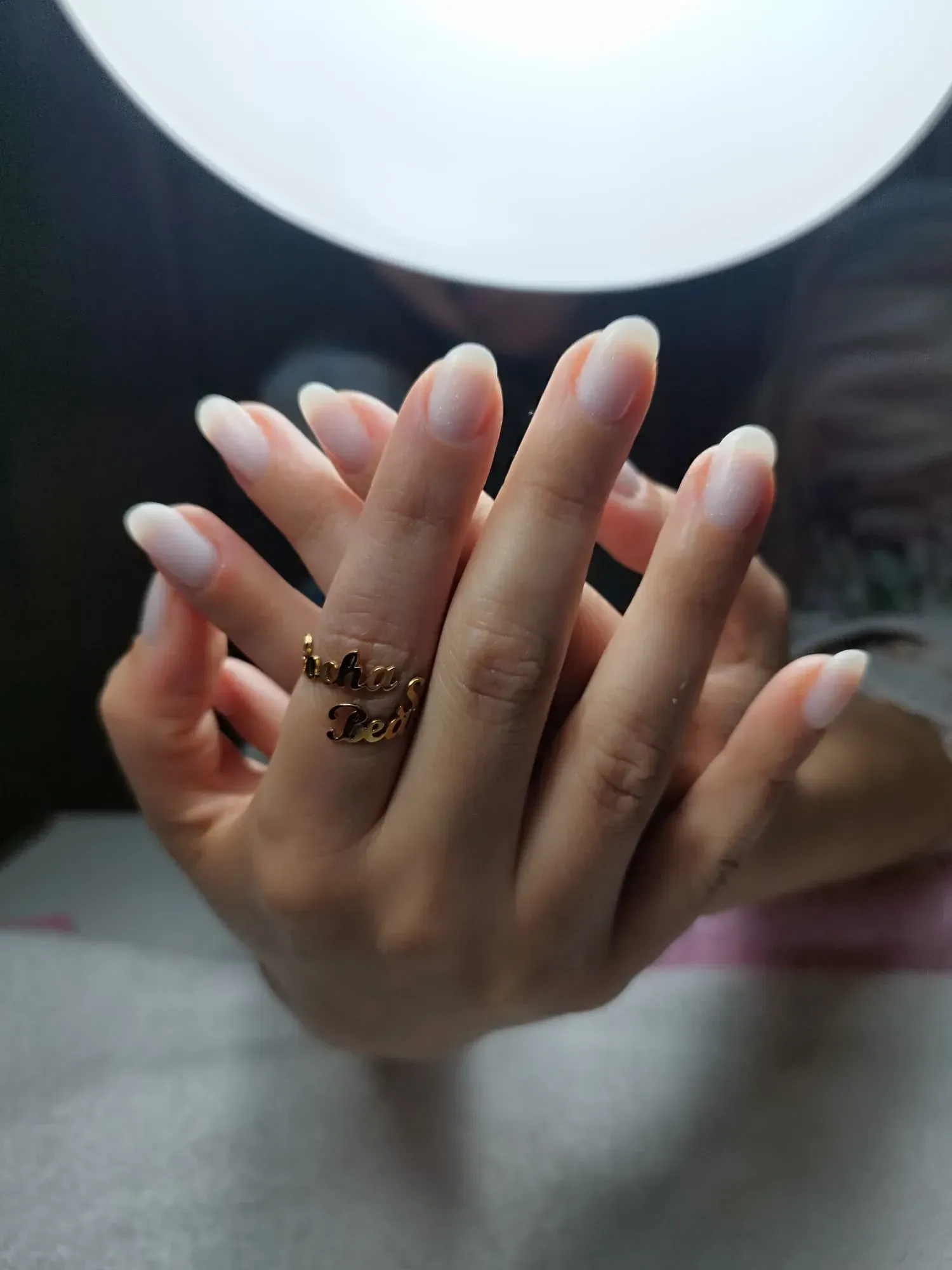 Manos con uñas largas y ovaladas, luciendo un anillo de oro, bajo una luz brillante.