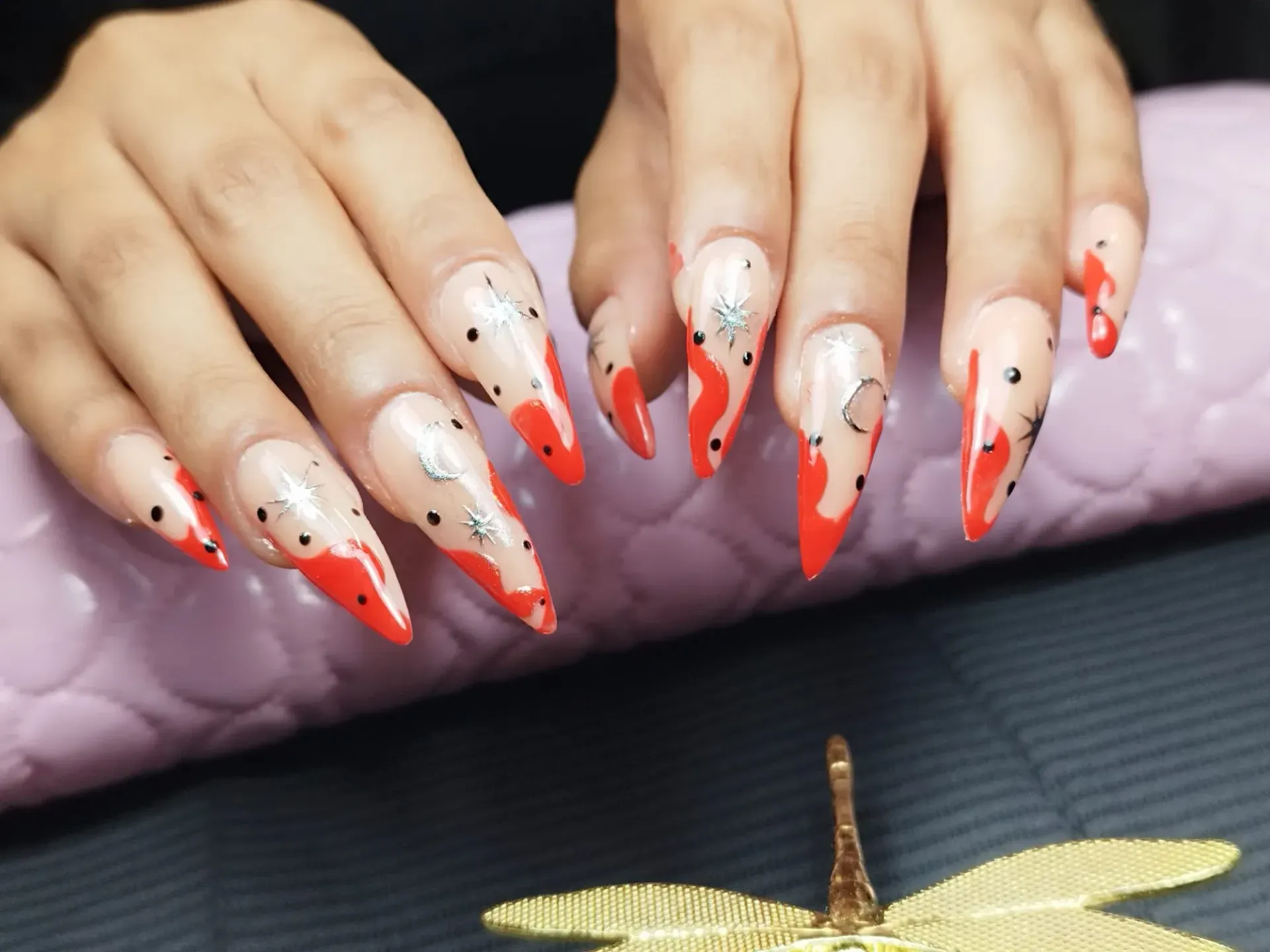 Uñas largas y puntiagudas con base transparente, puntas rojas y detalles plateados.