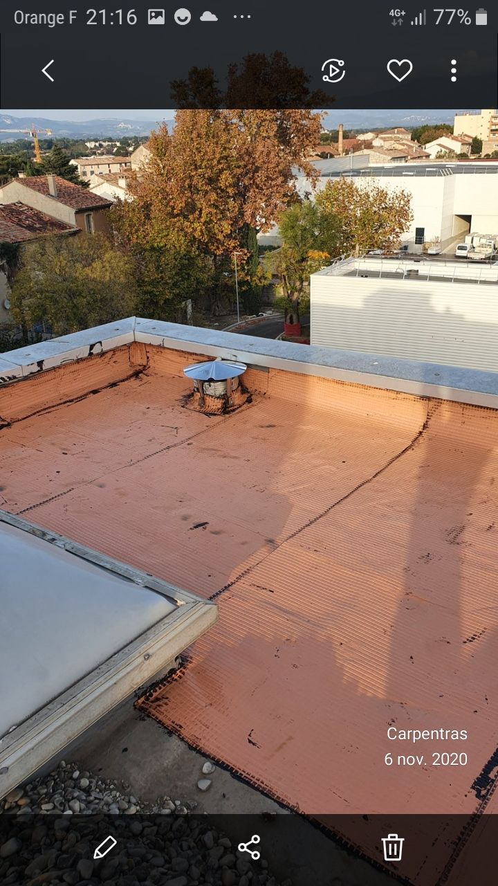 Terrasse sur le toit avec sol orange, murets blancs et un petit banc donnant sur les maisons et les arbres environnants.