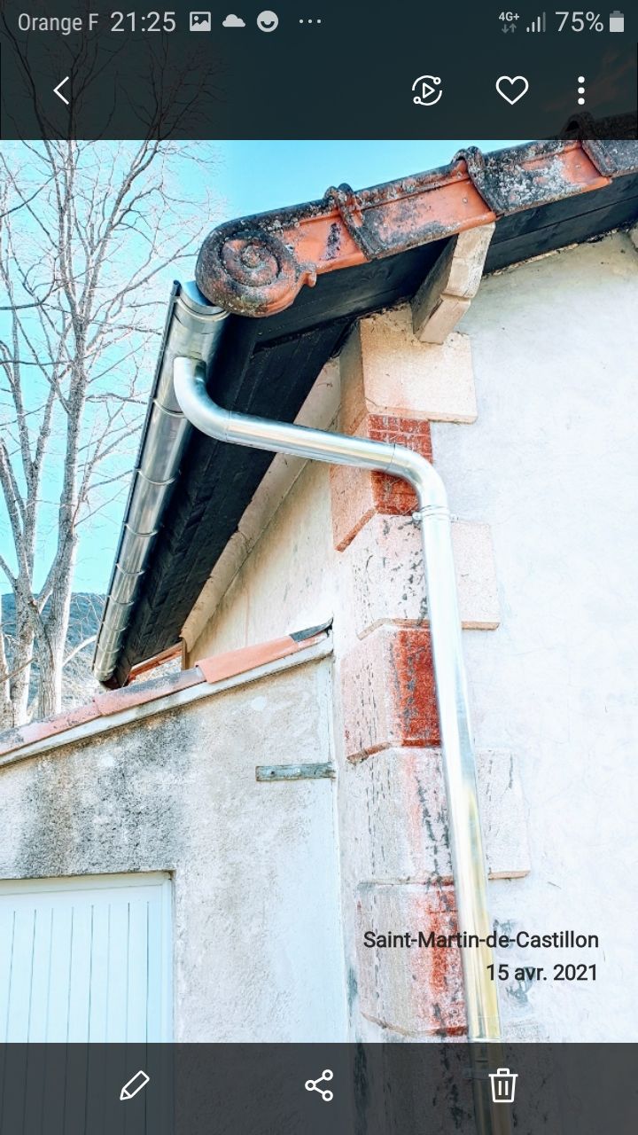 Gros plan sur une gouttière et une descente pluviale blanches, à côté d'un toit enneigé sur les avant-toits.