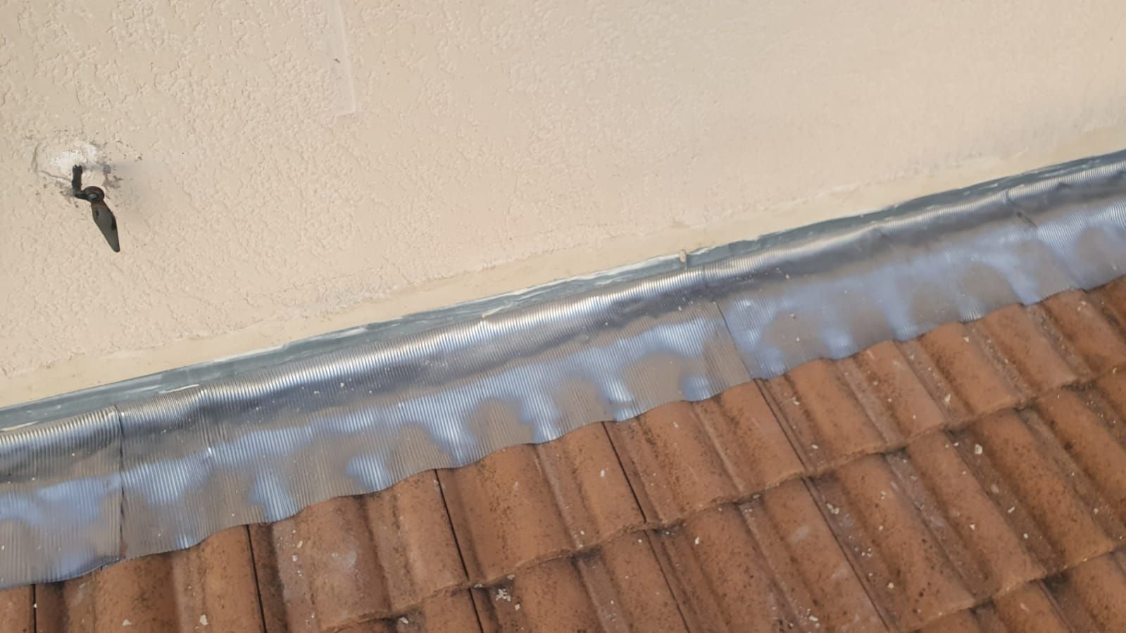 Bord de toit endommagé avec solin décollé à côté d'un mur beige et de bardeaux bruns.