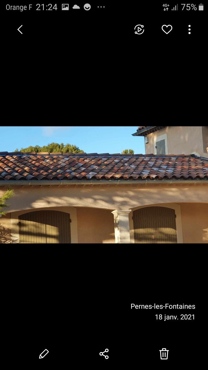 Toit de tuiles rouges et porche voûté d'une maison en stuc baignée de soleil sous un ciel bleu