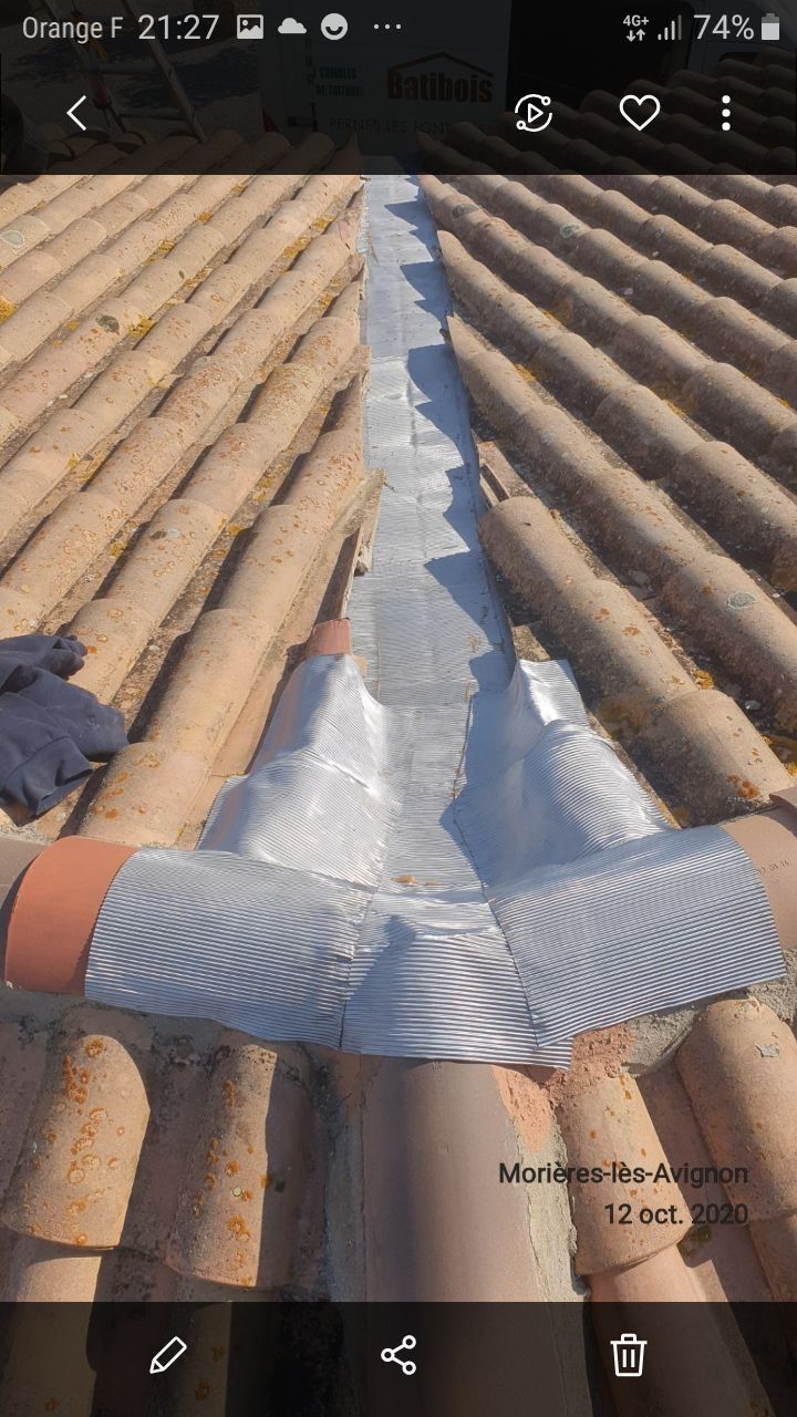 Toiture en tuiles de terre cuite avec un joint étanche argenté au centre.