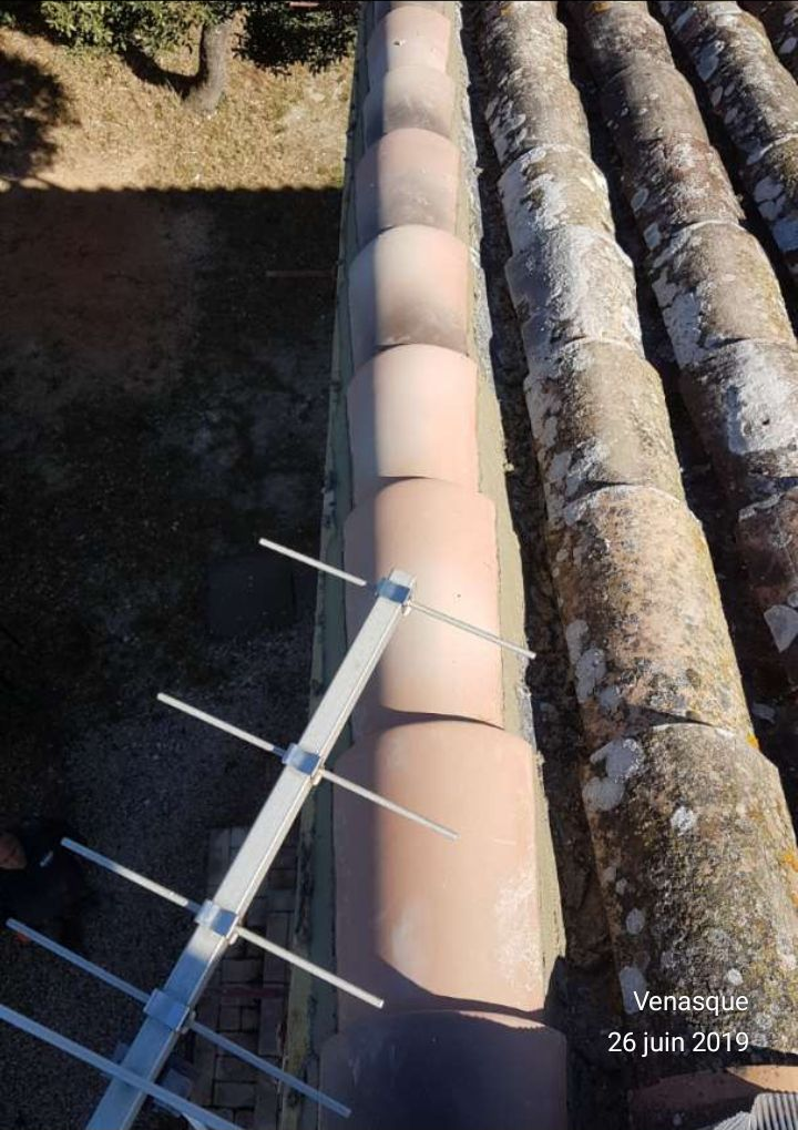 Vue depuis un toit-terrasse avec des tuyaux métalliques et un bras d'antenne parabolique, baigné de soleil.