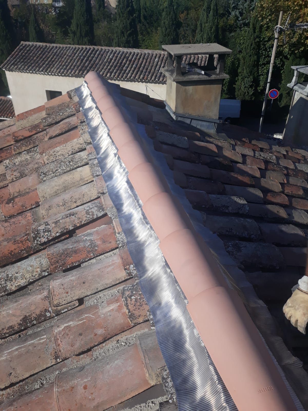 Faîtage avec solin rose neuf et mastic argenté brillant sur un toit de maison en tuiles.