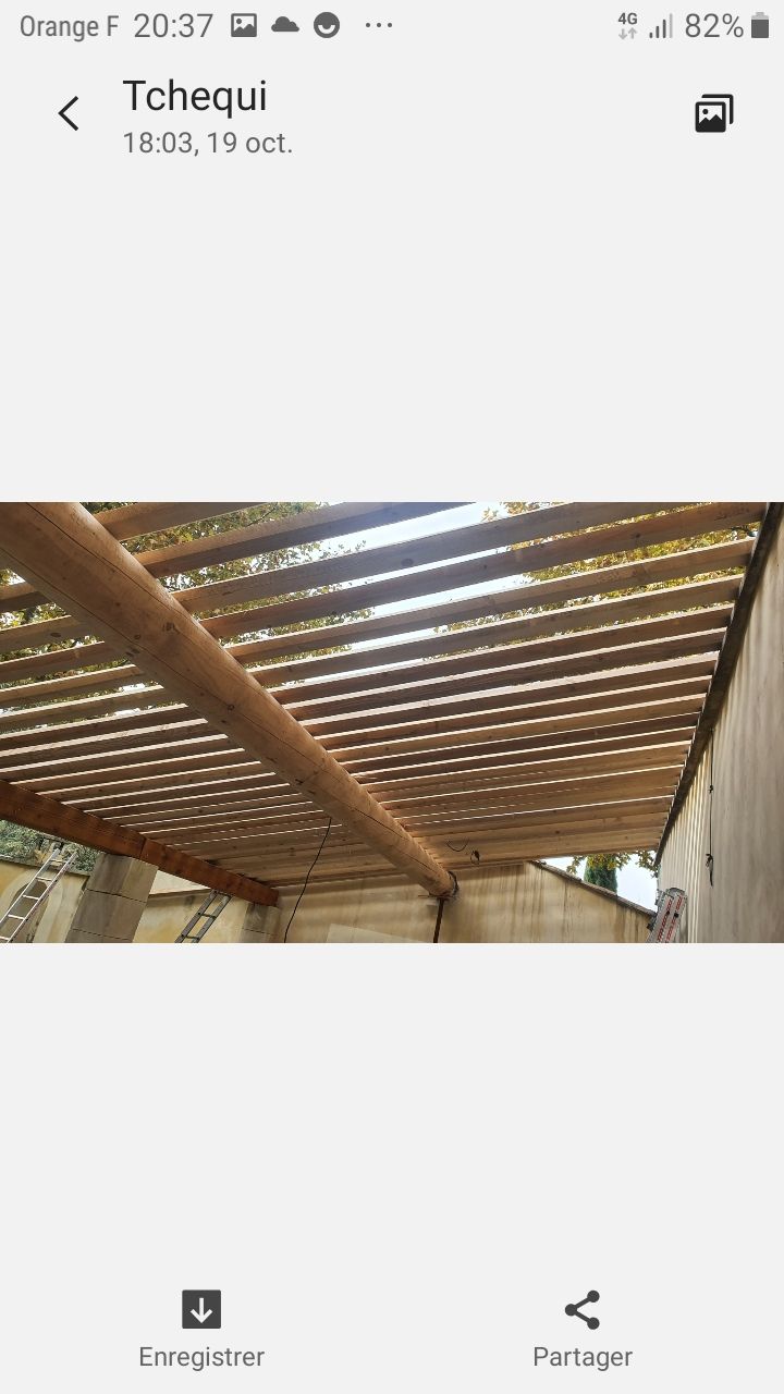 Vue intérieure d'un toit de hangar rustique avec poutres en bois et toiture métallique à claire-voie.