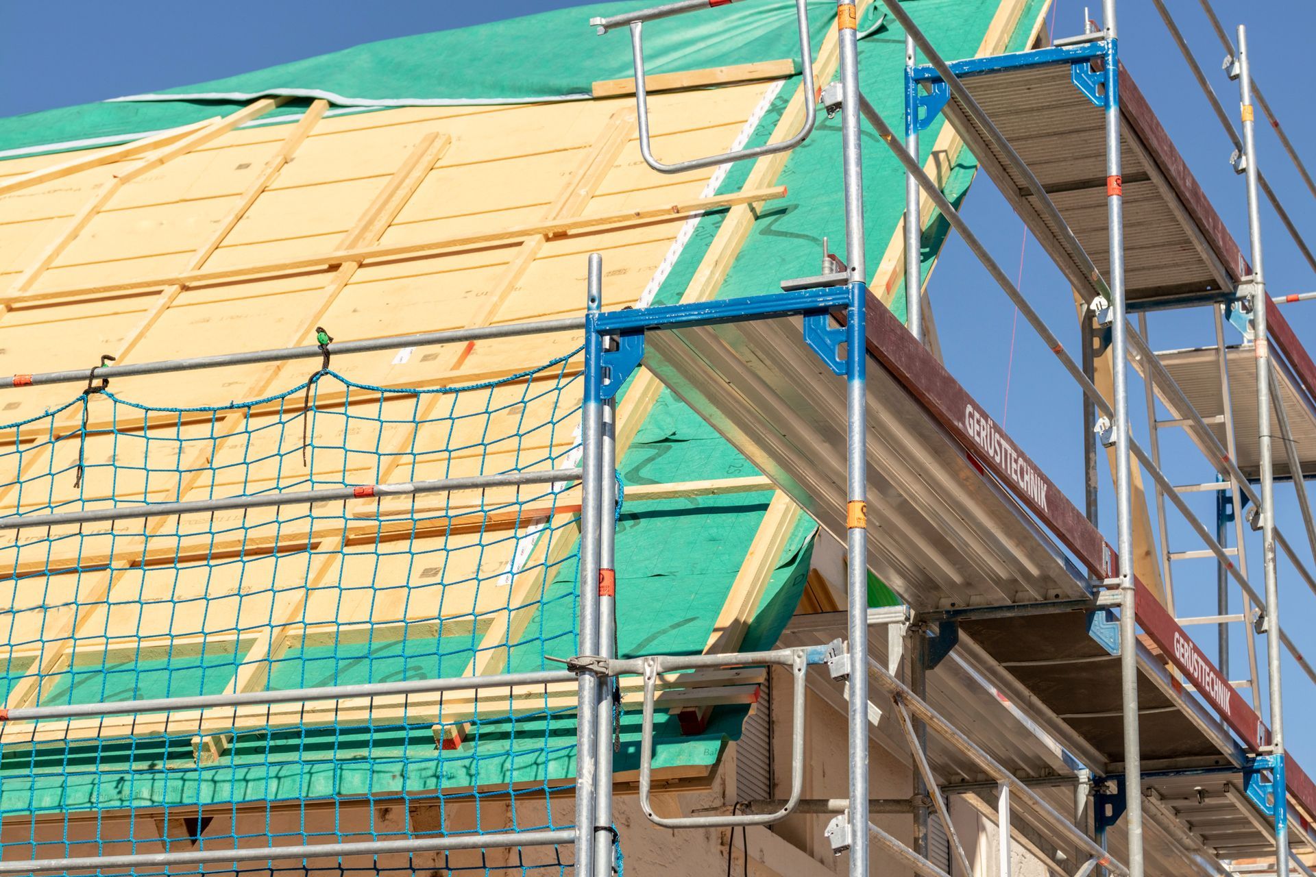 Échafaudages autour d'un bâtiment en construction, recouverts de bâches de protection vertes et beiges.