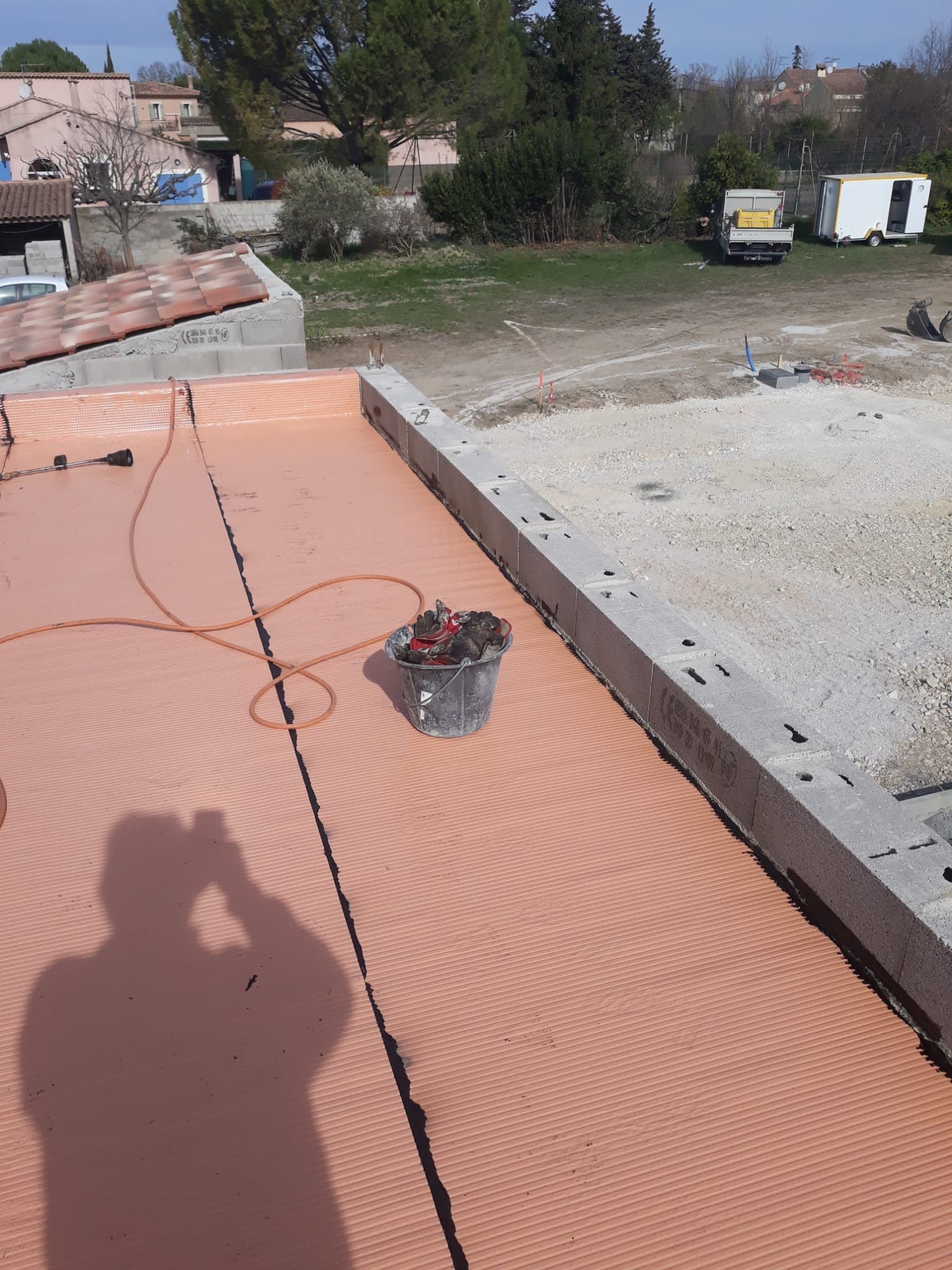 Toiture en construction avec panneaux isolants orange, bords en béton et un seau sur le toit.
