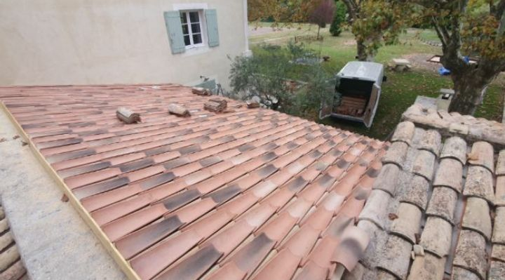 Deux toits de tuiles rouges mitoyens à côté d'une maison, avec une fenêtre et des chaises de patio en arrière-plan.
