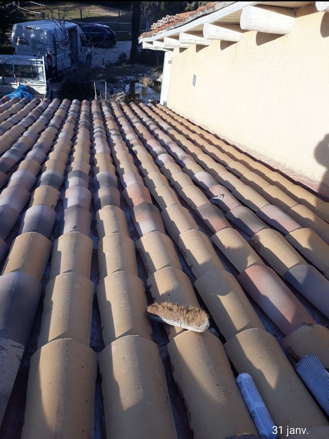 Toit-terrasse avec des rangées de tuiles brunes incurvées, jouxtant un mur blanc baigné de lumière naturelle.
