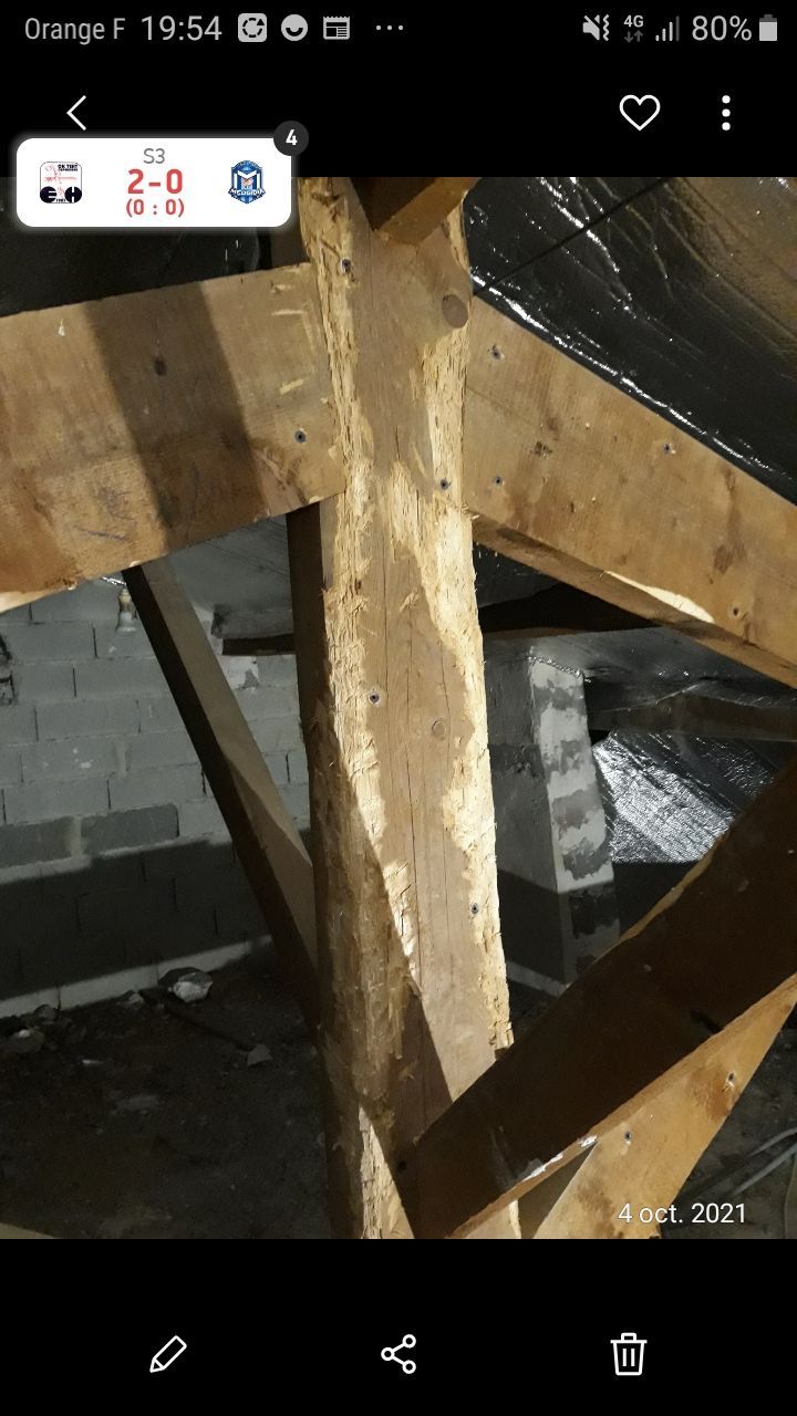 Gros plan sur une poutre en bois endommagée et ses supports dans un grenier ou un vide sanitaire.