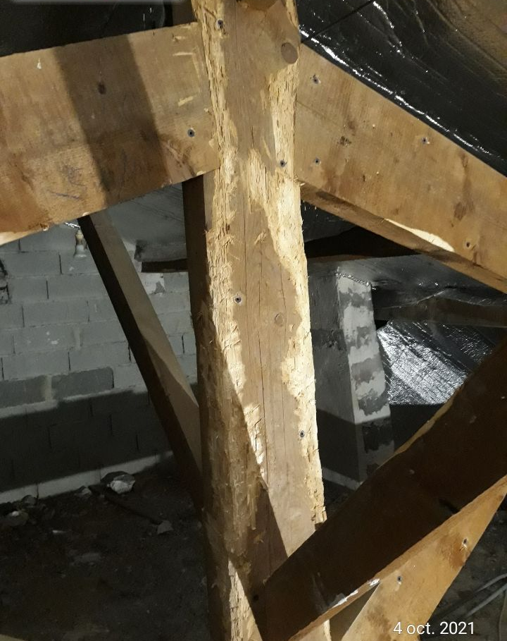 Gros plan sur une poutre en bois brut et sa structure de support dans un grenier ou un vide sanitaire sombre.