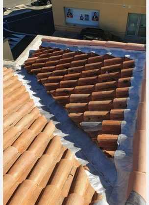 Des tuiles de toit en terre cuite disposées en motif triangulaire sur une bâche bleue dans un atelier.