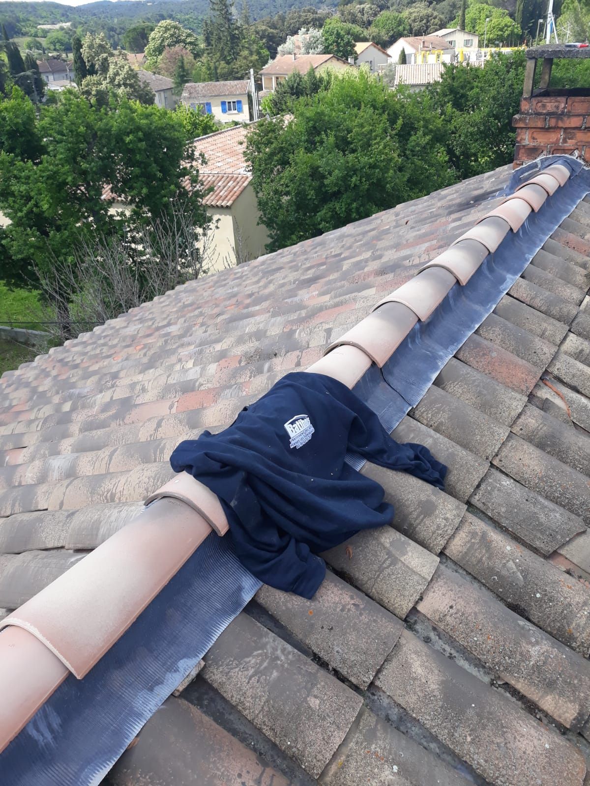 Un sweat-shirt bleu foncé drapé sur le faîte d'un toit, avec des bardeaux gris et des arbres verts en arrière-plan.