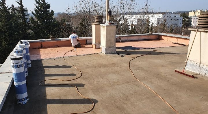 Terrasse sur le toit avec sol en béton, canalisations et une personne accroupie près du mur du fond.