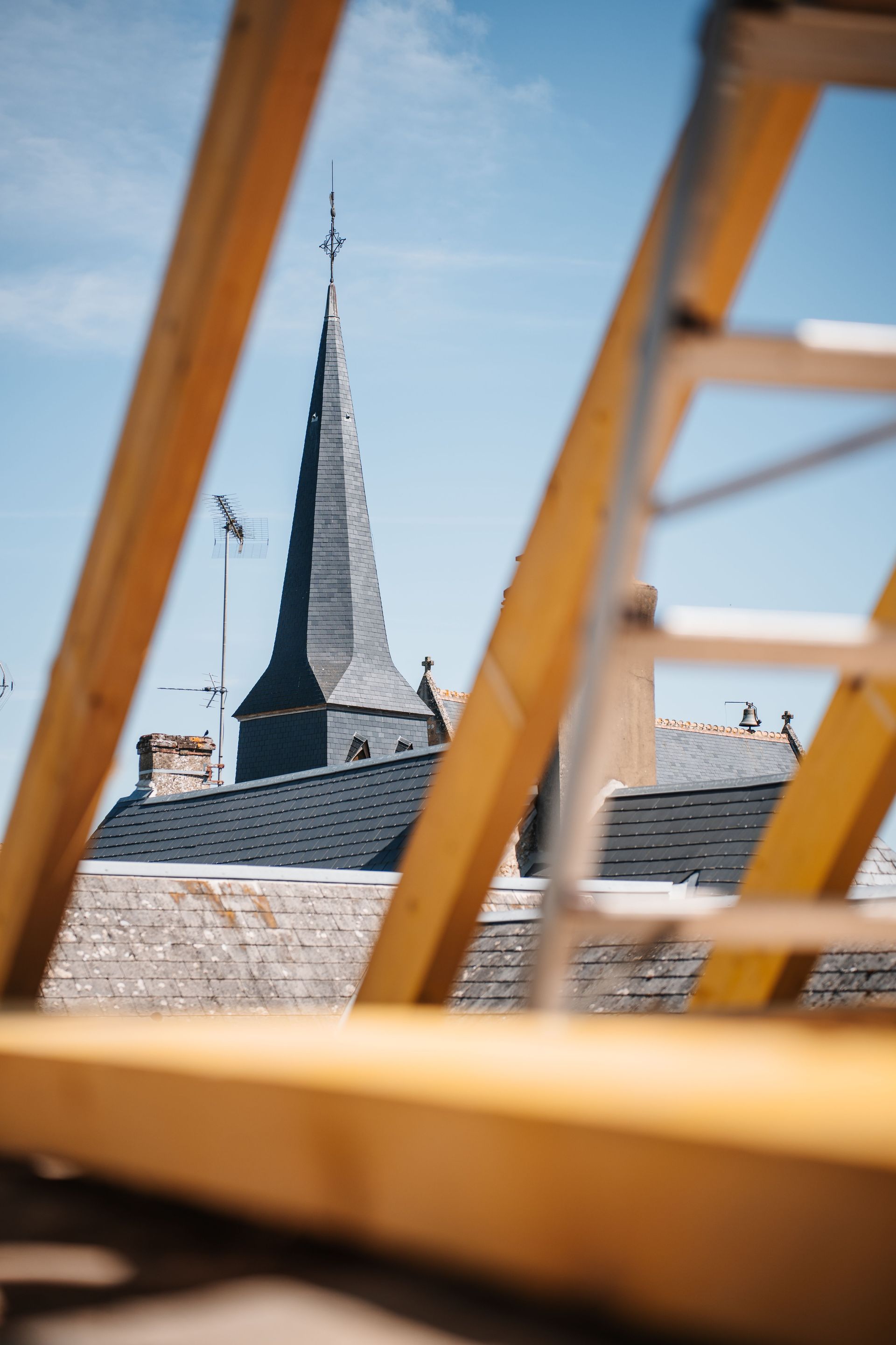 Clocher d'église et toits aperçus à travers des poutres en bois sur un ciel bleu