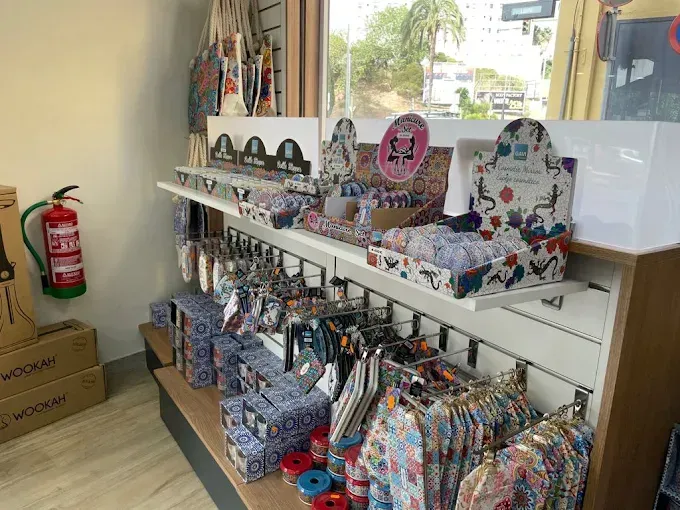 Dentro de una tienda, se exhiben regalos: papelería, bolsos y ropa. Extintor en la pared.