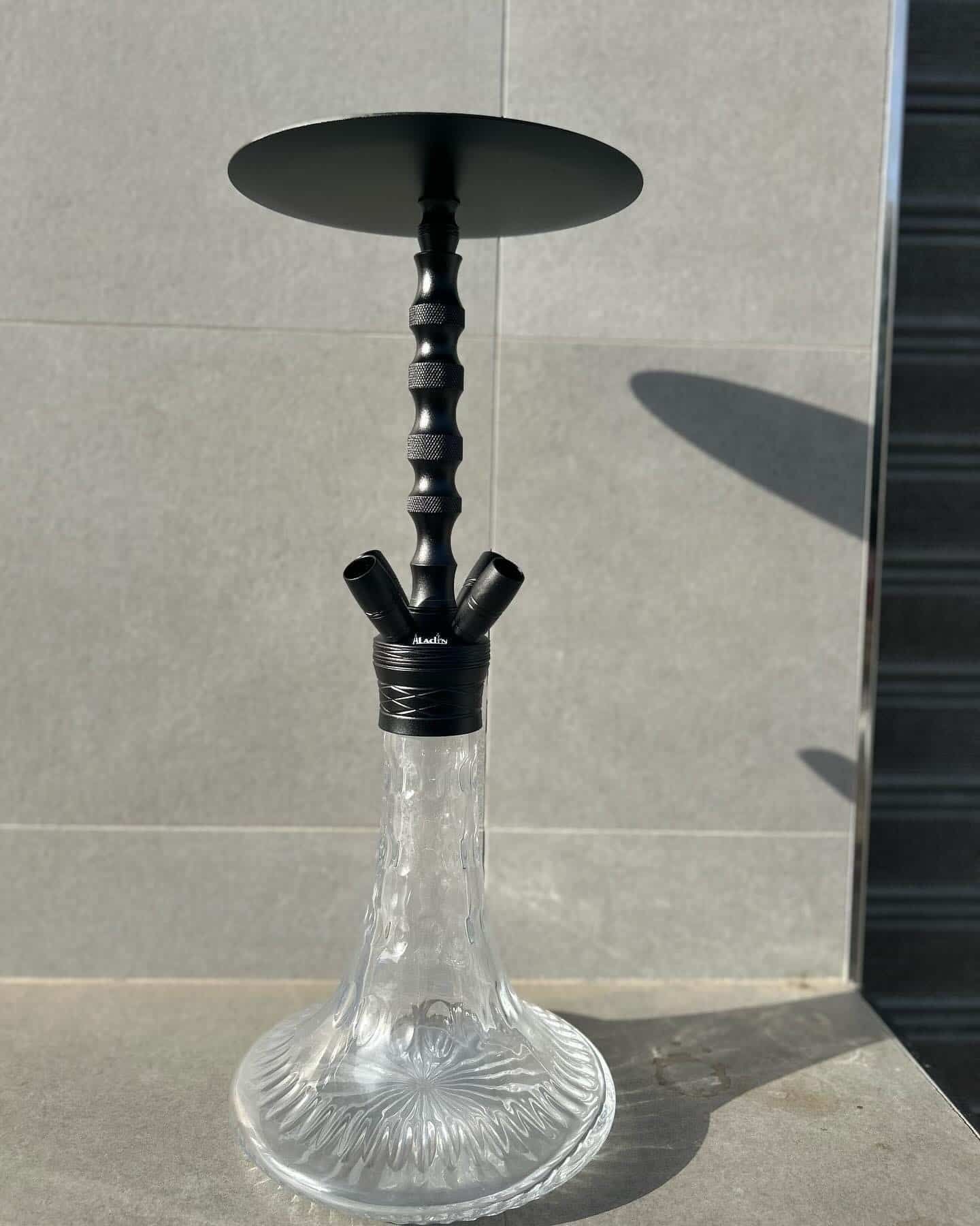 Cachimba negra con base de cristal, colocada contra una pared de azulejos.