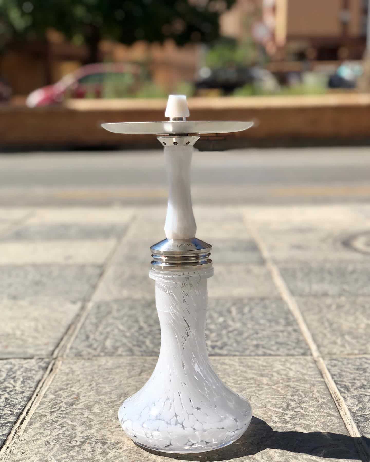 Cachimba blanca con detalles plateados, al aire libre, sobre una superficie de piedra.