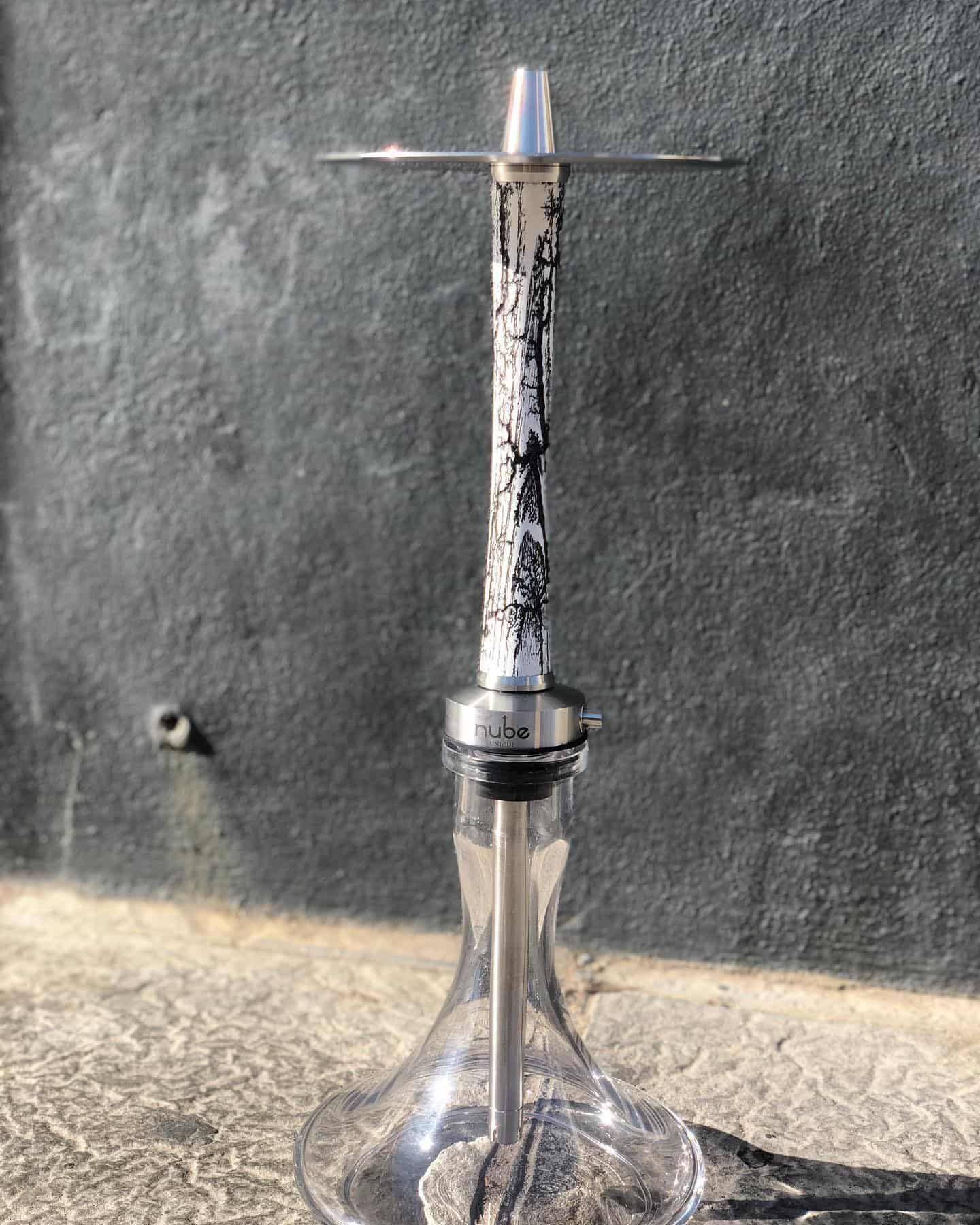 Cachimba plateada con tallo decorativo y base de cristal sobre fondo gris.