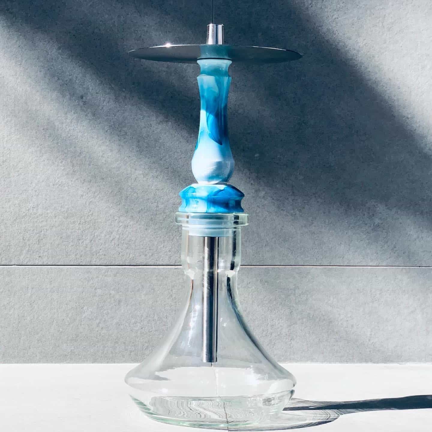 Cachimba azul y blanca con base de vidrio transparente, sobre un fondo gris.