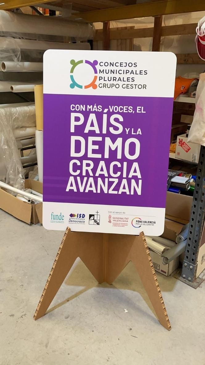 Cartel blanco y morado sobre soporte de cartón; texto en español promoviendo el país y la democracia.