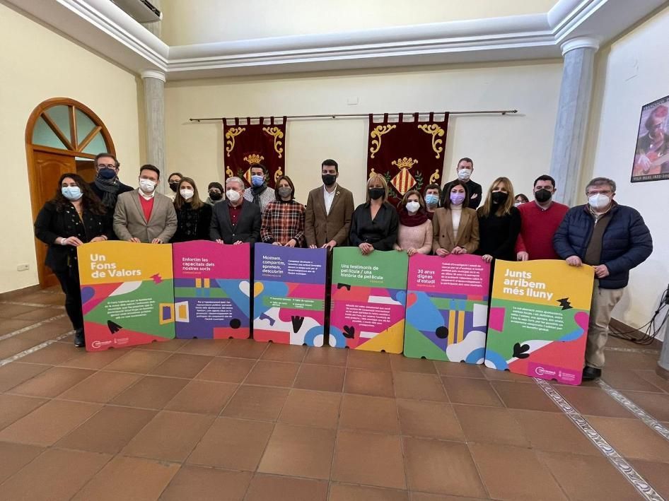 Grupo de personas sosteniendo carteles coloridos en el interior, posiblemente un anuncio de evento.