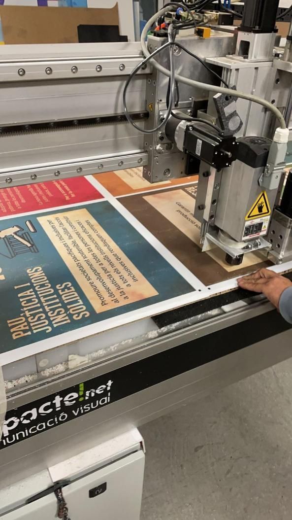 Una gran máquina de impresión corta un póster. La máquina es blanca y gris, y el póster tiene secciones azules.