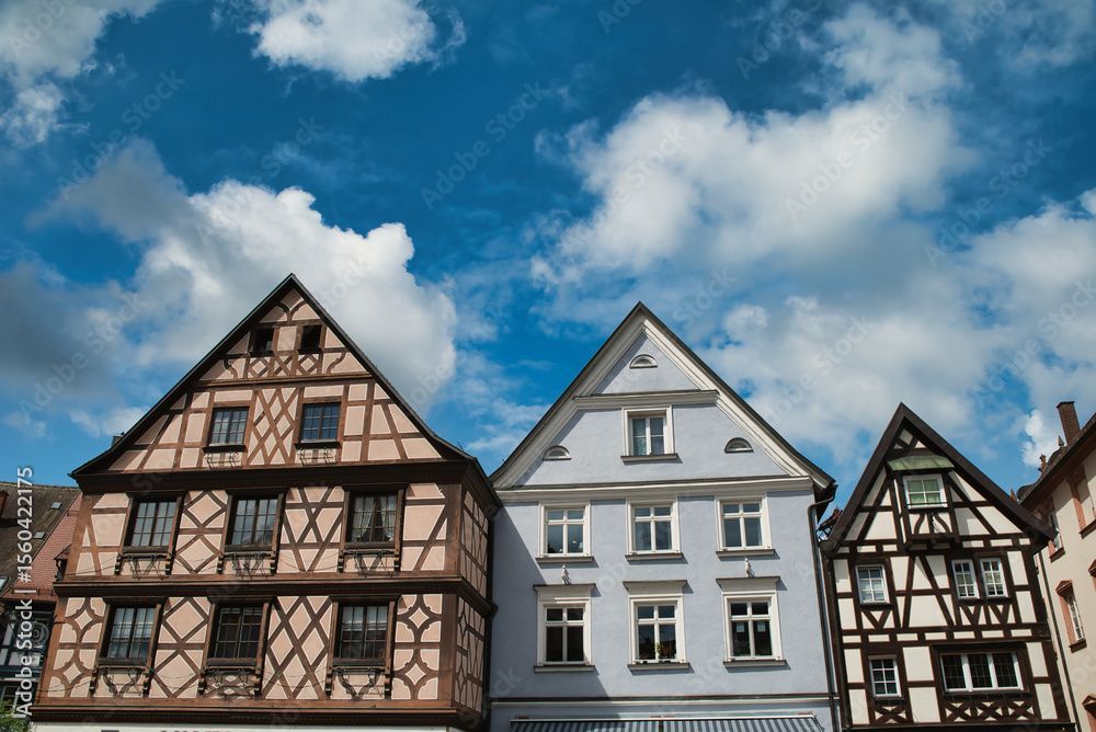 Fachwerkhäuser mit Giebeldächern unter blauem Himmel mit Wolken.