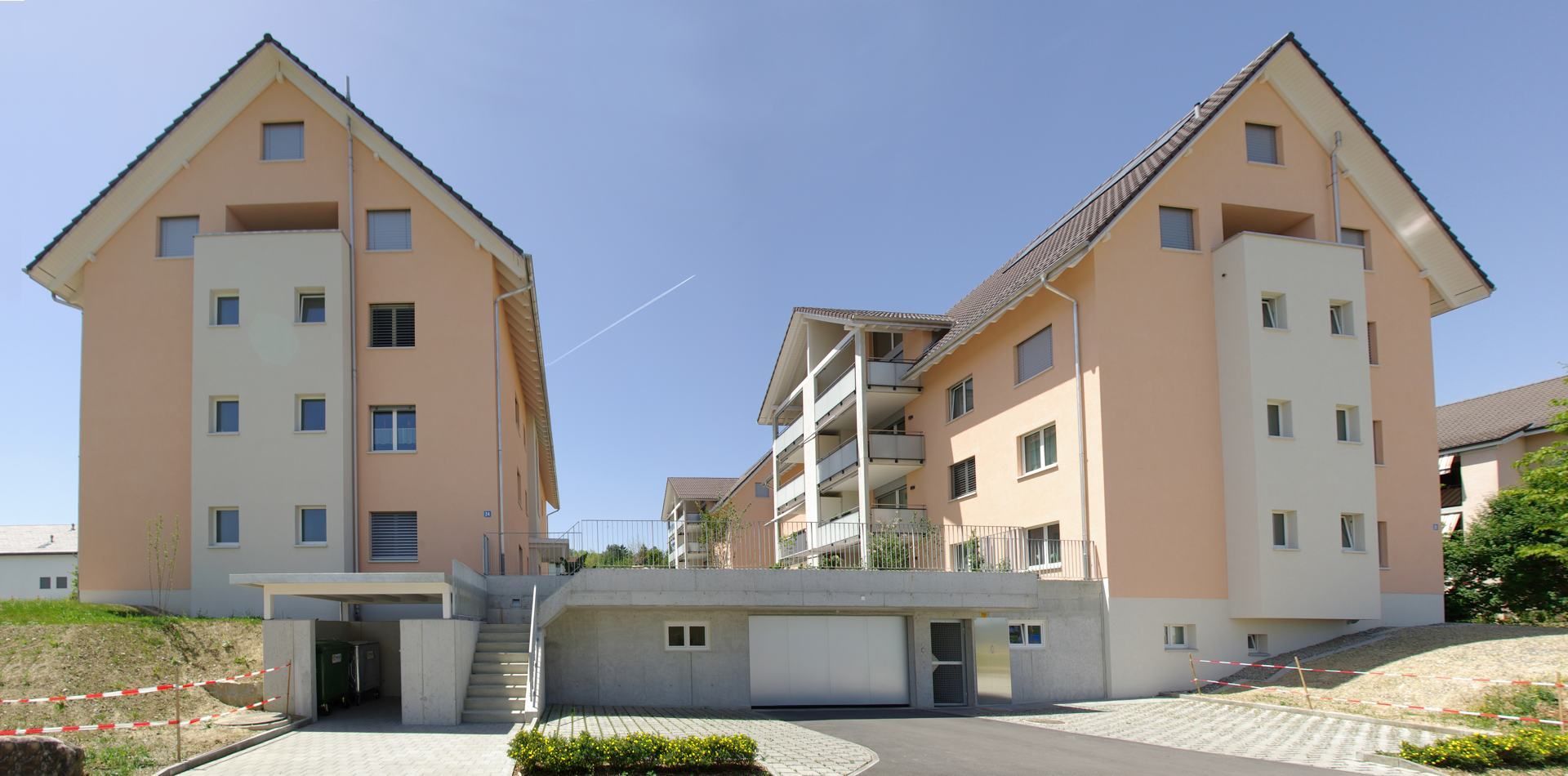 Mehrstöckige Wohnhäuser mit hellpfirsichfarbenen Wänden und dunklen Dächern vor blauem Himmel.