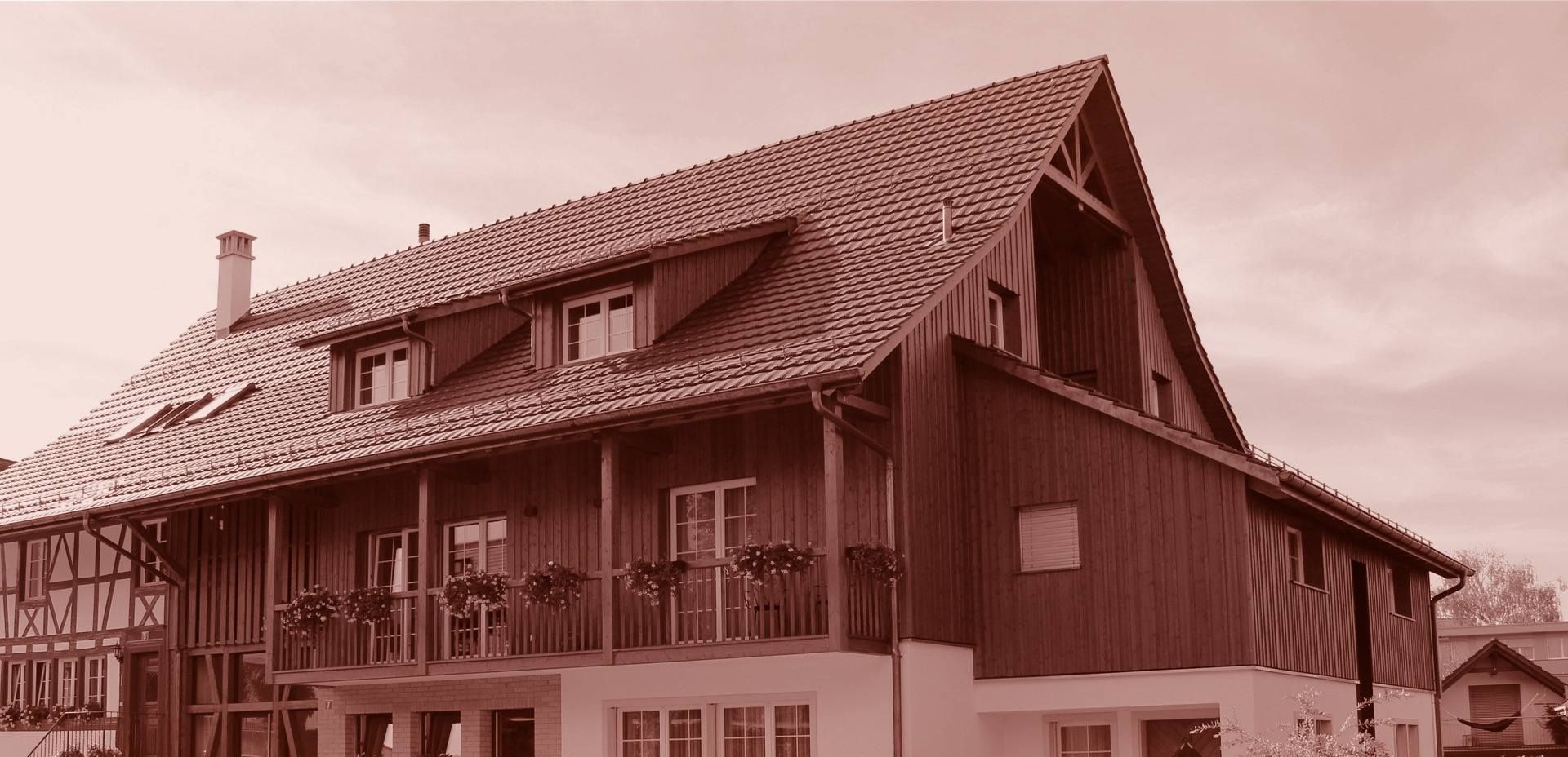 Eine Reihe moderner Häuser mit dunklen und roten Backsteinfassaden. Im Vordergrund eine grasbewachsene Wiese.