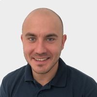 Ein Mann mit Glatze, blauen Augen und einem dunkelblauen Poloshirt lächelt.