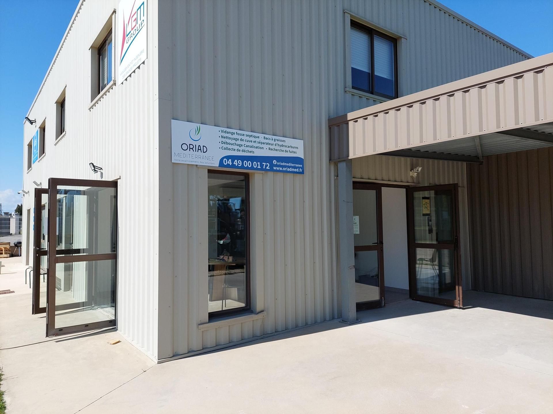 Extérieur du bâtiment avec bardage métallique, fenêtres et auvent au-dessus de l'entrée.