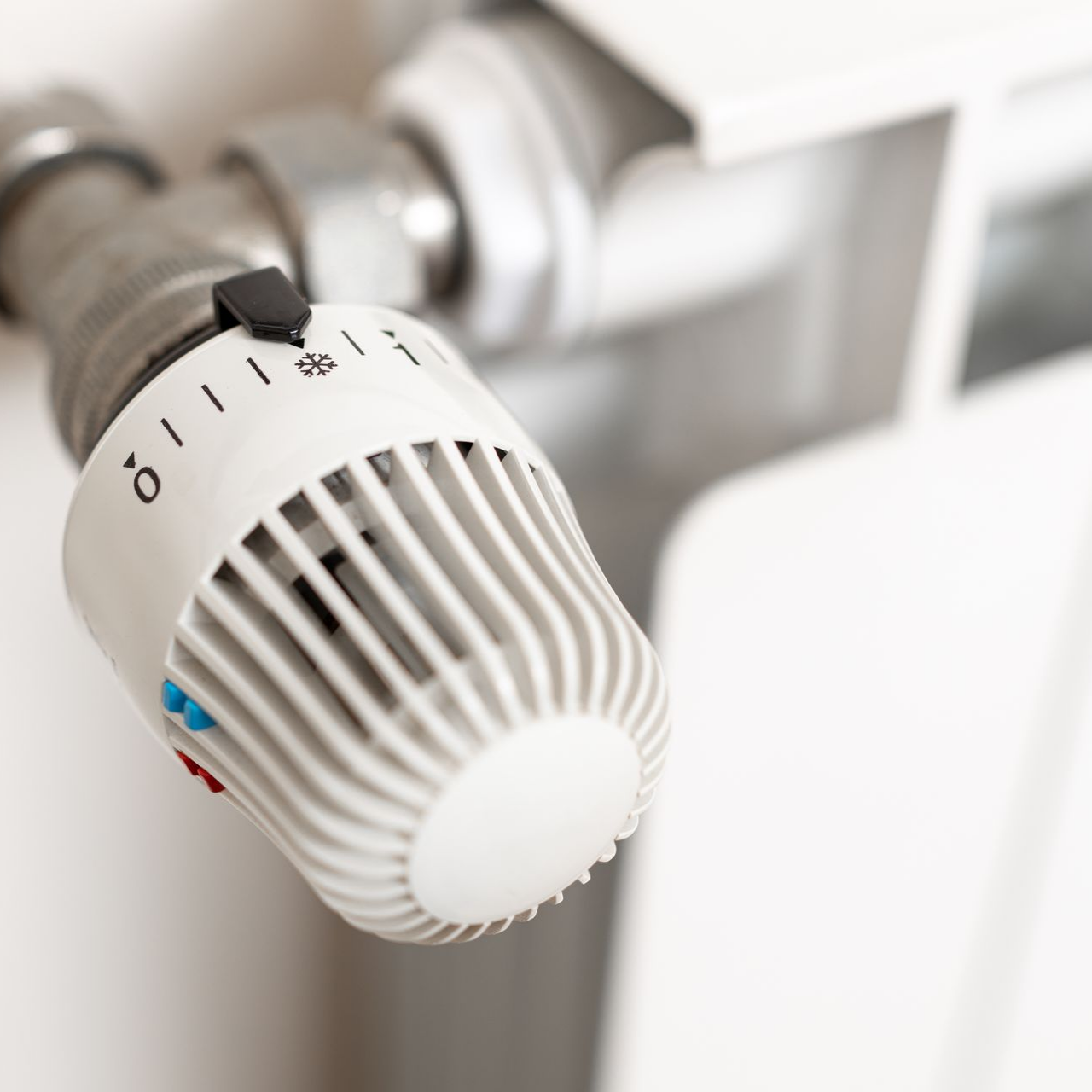 Gros plan sur un thermostat de radiateur blanc avec réglages numérotés et un bouton de commande noir.