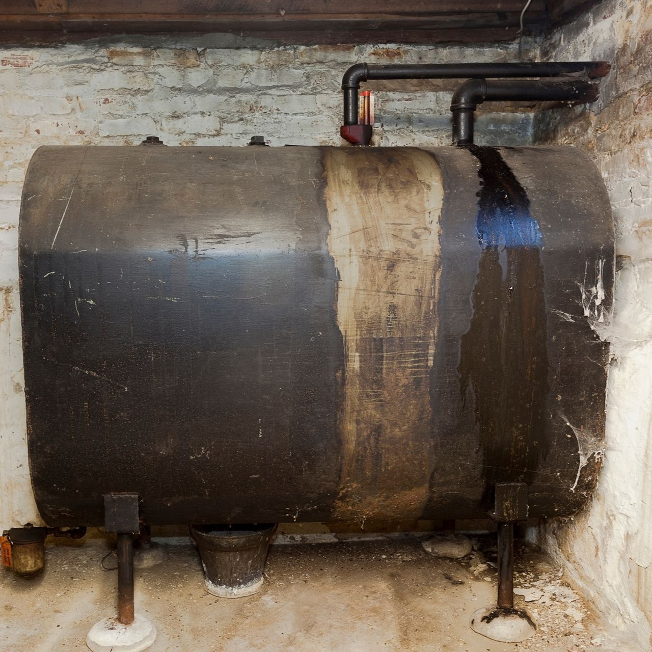 Cuve à mazout au sous-sol, en métal sombre, avec tuyaux et murs en briques.