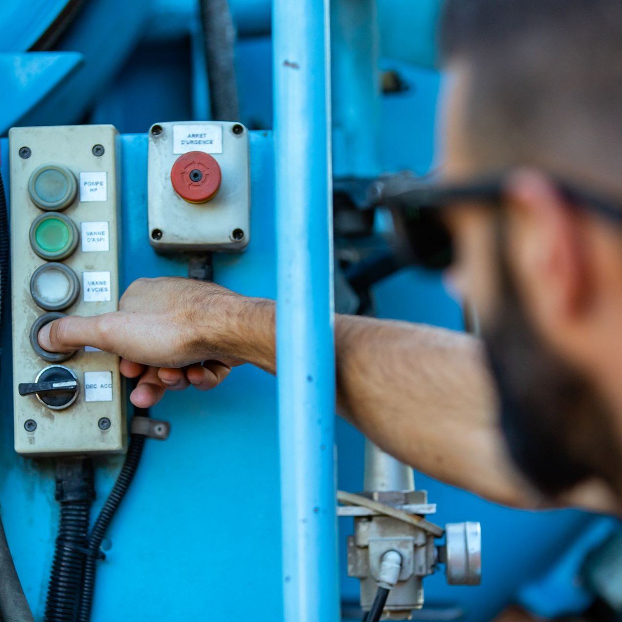 Une personne appuie sur un bouton d'un panneau de commande industriel bleu.