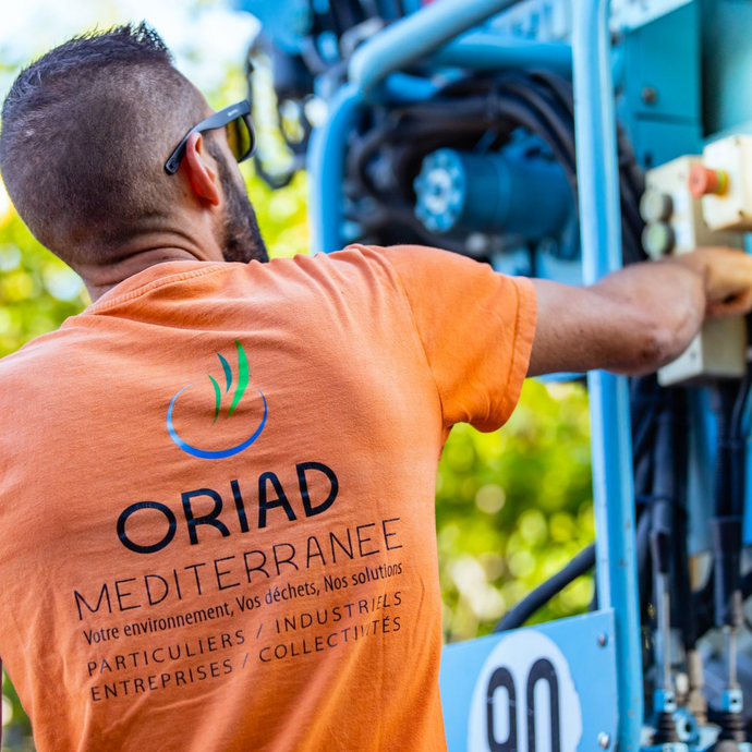 Un homme en tee-shirt orange avec le logo travaille sur une machine bleue.
