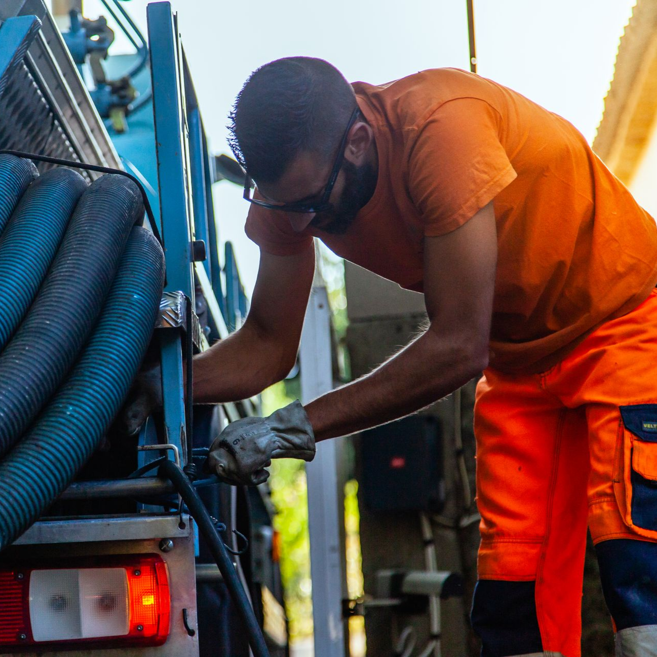Un homme en tenue de travail orange travaille sur un camion.
