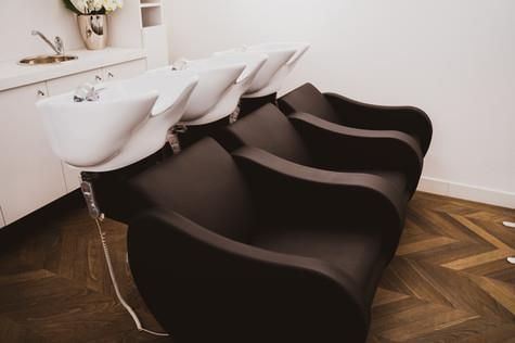 Eine Reihe von Friseurstühlen mit Waschbecken in einem Raum.