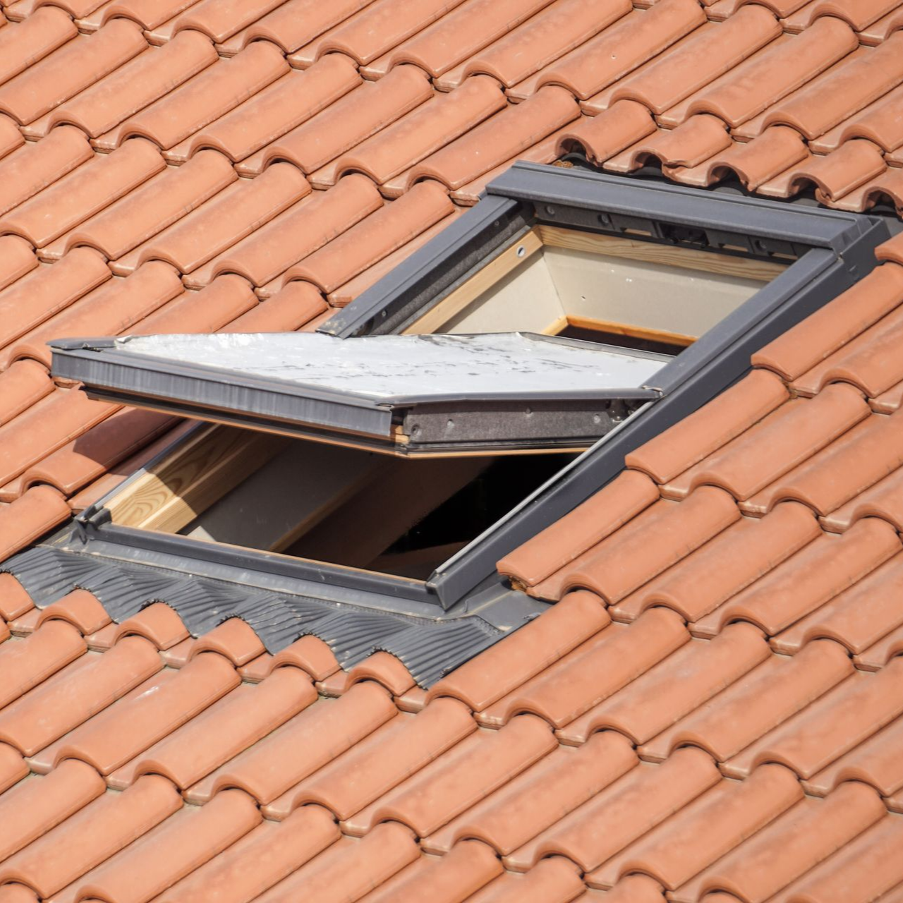 Puits de lumière ouvert sur un toit de tuiles en terre cuite, incliné vers le haut, laissant entrer la lumière du soleil.