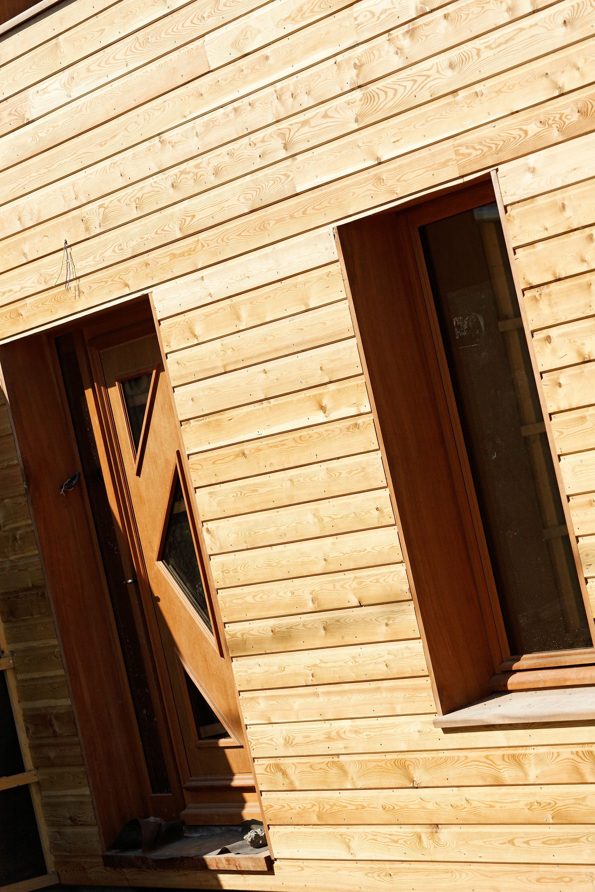 Extérieur de bâtiment en bois avec porte et fenêtre ; bardage horizontal en bois, cadres de porte et de fenêtre bruns.