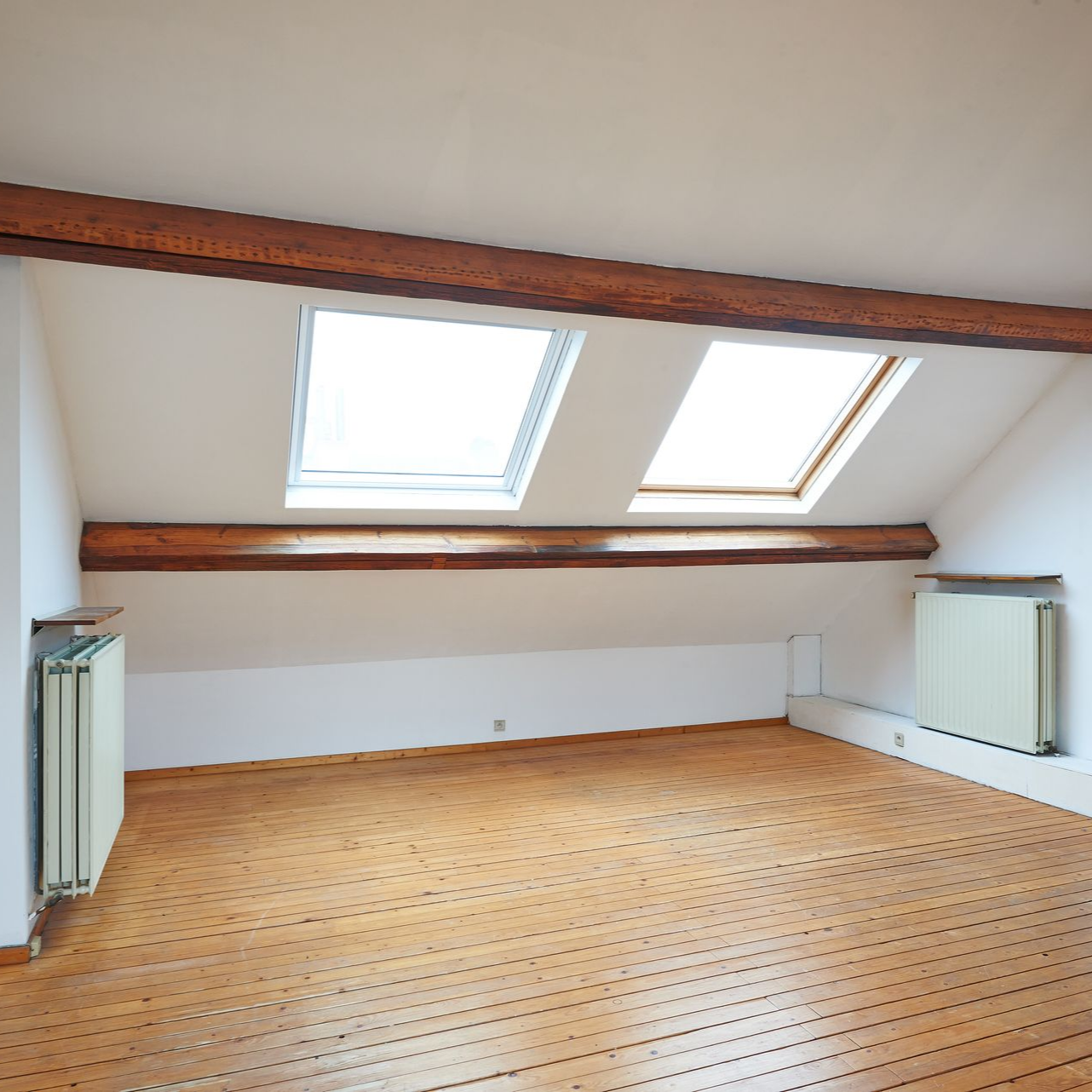 Grenier aménagé vide avec parquet, puits de lumière et poutres apparentes.
