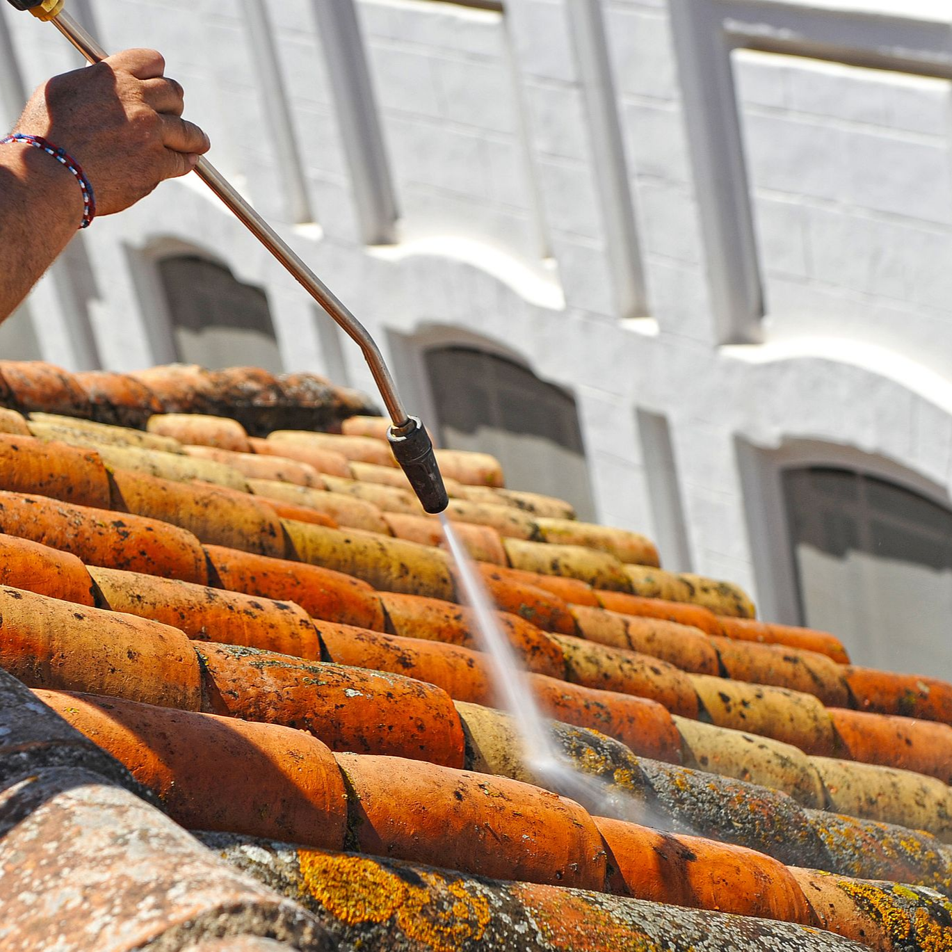 Une personne nettoie à haute pression un toit de tuile rouge.