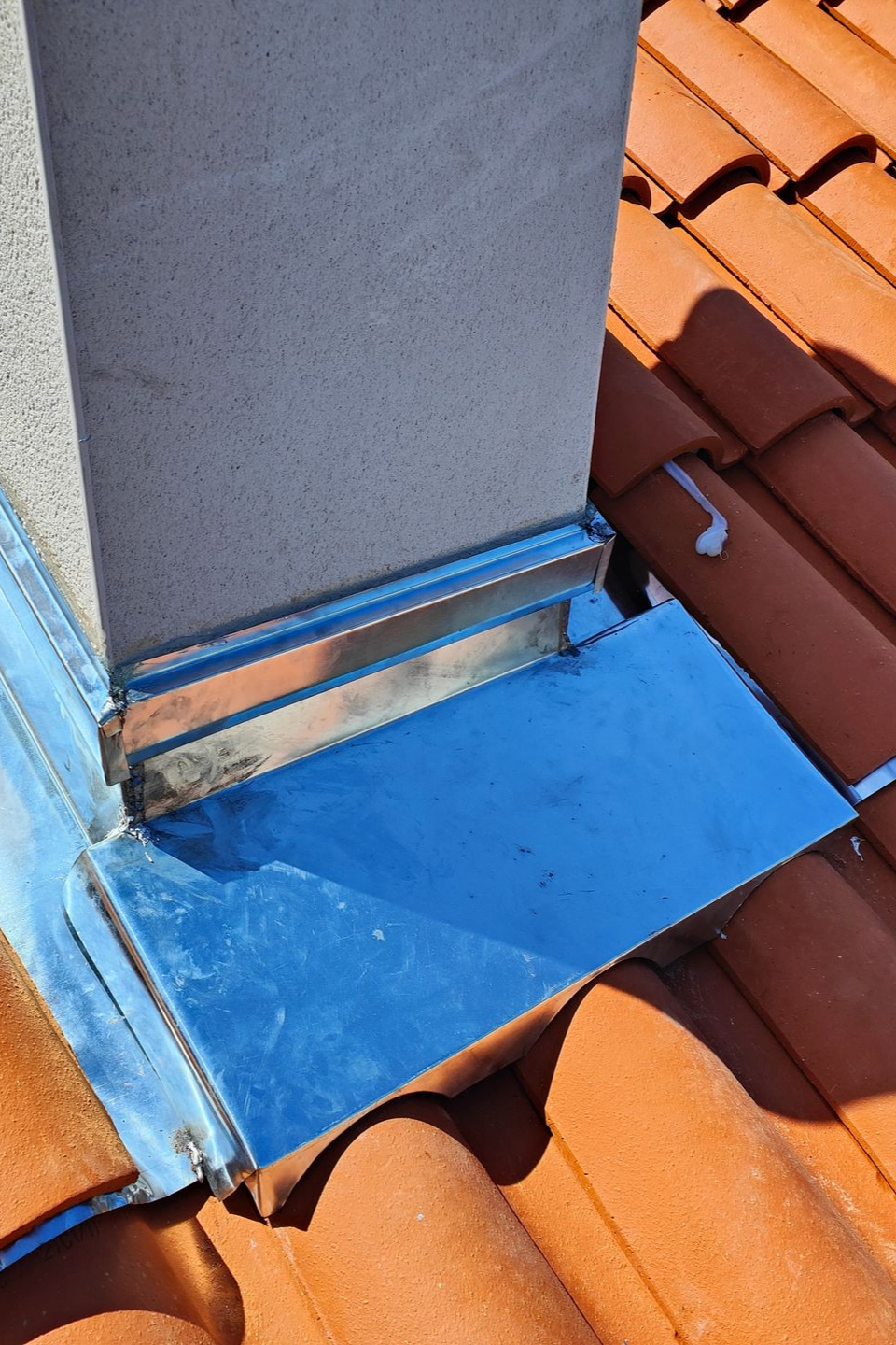 Solin métallique autour d'une cheminée sur un toit de tuiles rouges, assurant la protection contre les infiltrations d'eau.