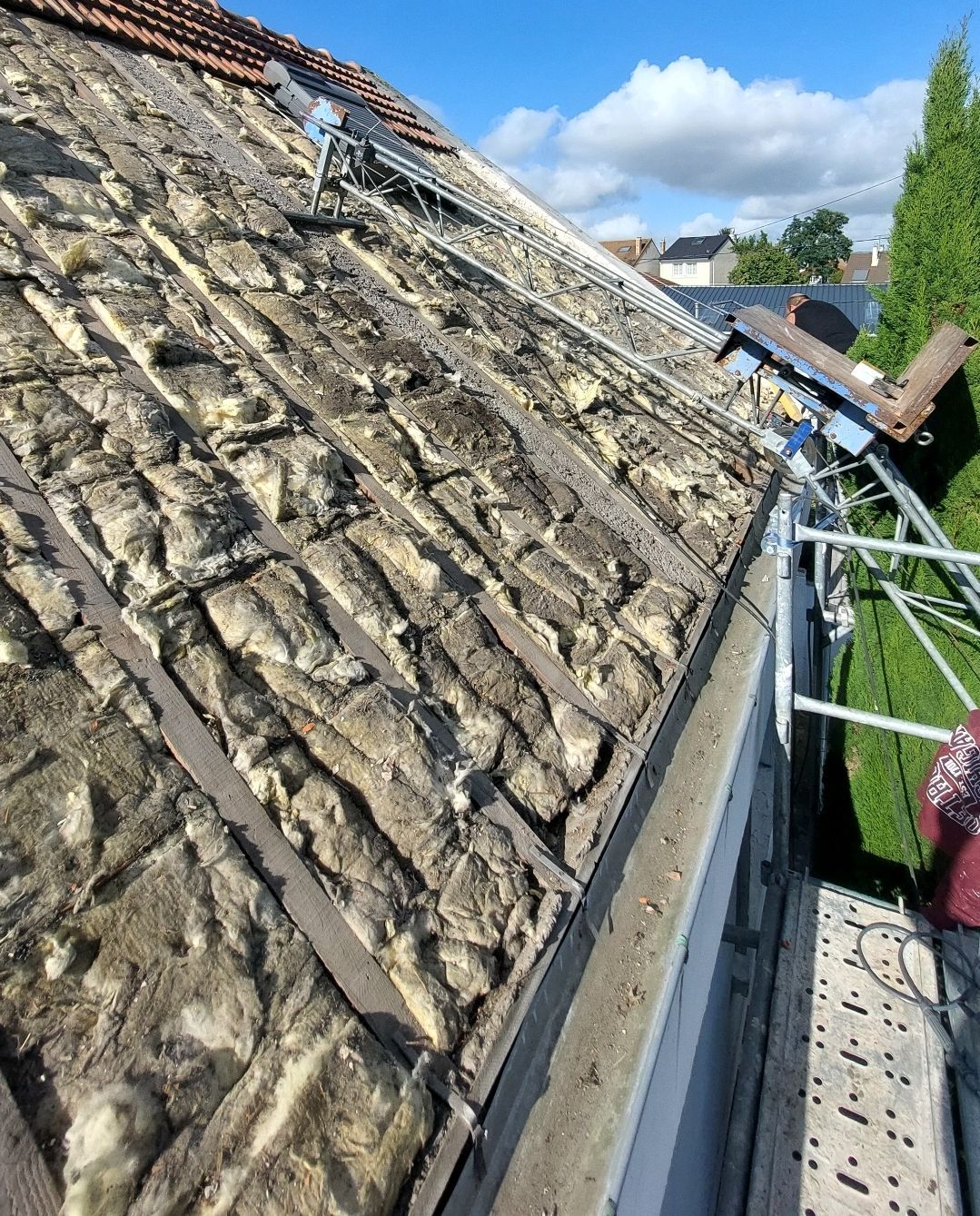 Toiture partiellement découverte, laissant apparaître l'isolation. Des échafaudages soutiennent les travaux en cours.